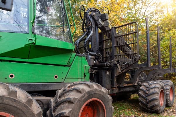 Heavy forestry machine with muddy tires, crane, grapple, and metal frame stands on autumn woodland trail.