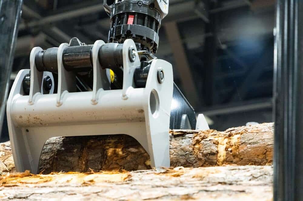 eavy machinery claw is gripping a log in an industrial environment with visible wood textures and details.