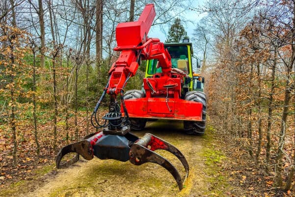 A large red machine moves on a dirt path between trees, preparing the area for landscaping or clearing tasks.