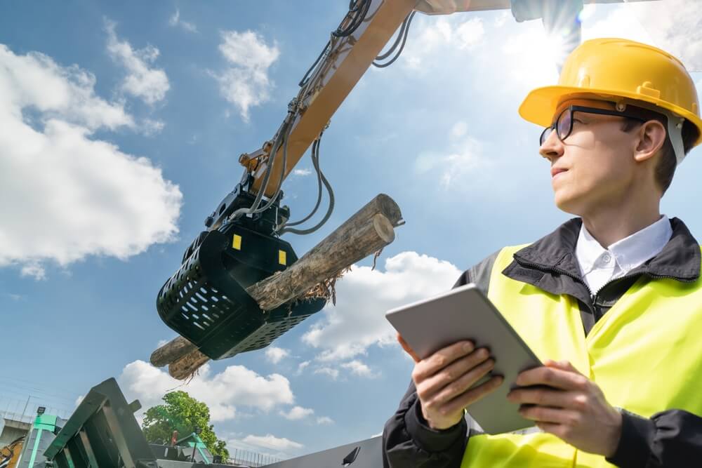 Worker with digital tablet controls process of loading timber.