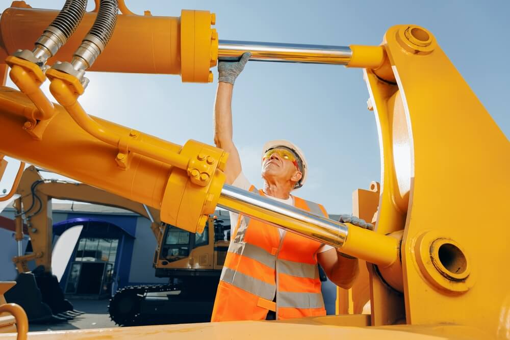 Machinery tractor mechanic checks hydraulic hose system equipment on excavator.
